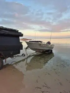 A 4m tinny being launched from a beach into calm morning waters in Shark Bay, Western Australia